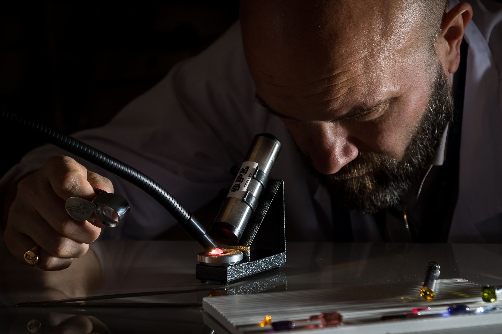 A jewellery valuer examining a gemstone by torchlight with a loupe